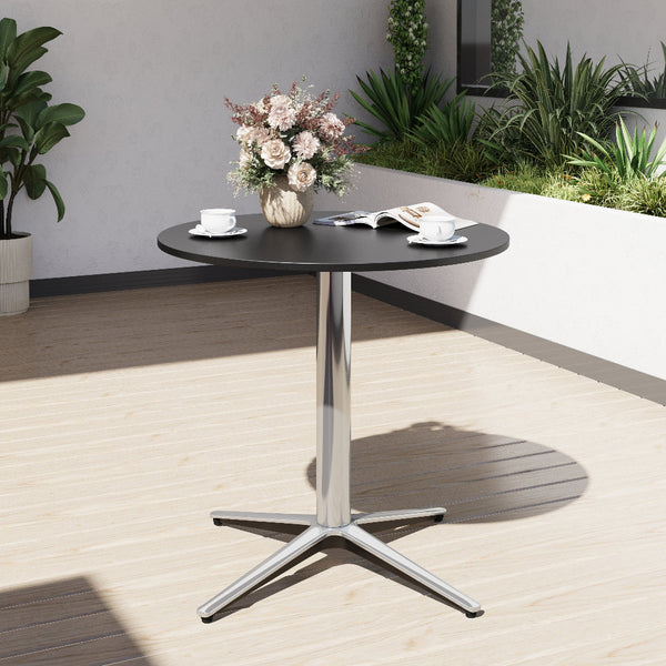 Round black table with a metallic base on a wooden deck, featuring a vase of flowers and books.