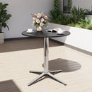 Round black table with a metallic base on a wooden deck, featuring a vase of flowers and books.