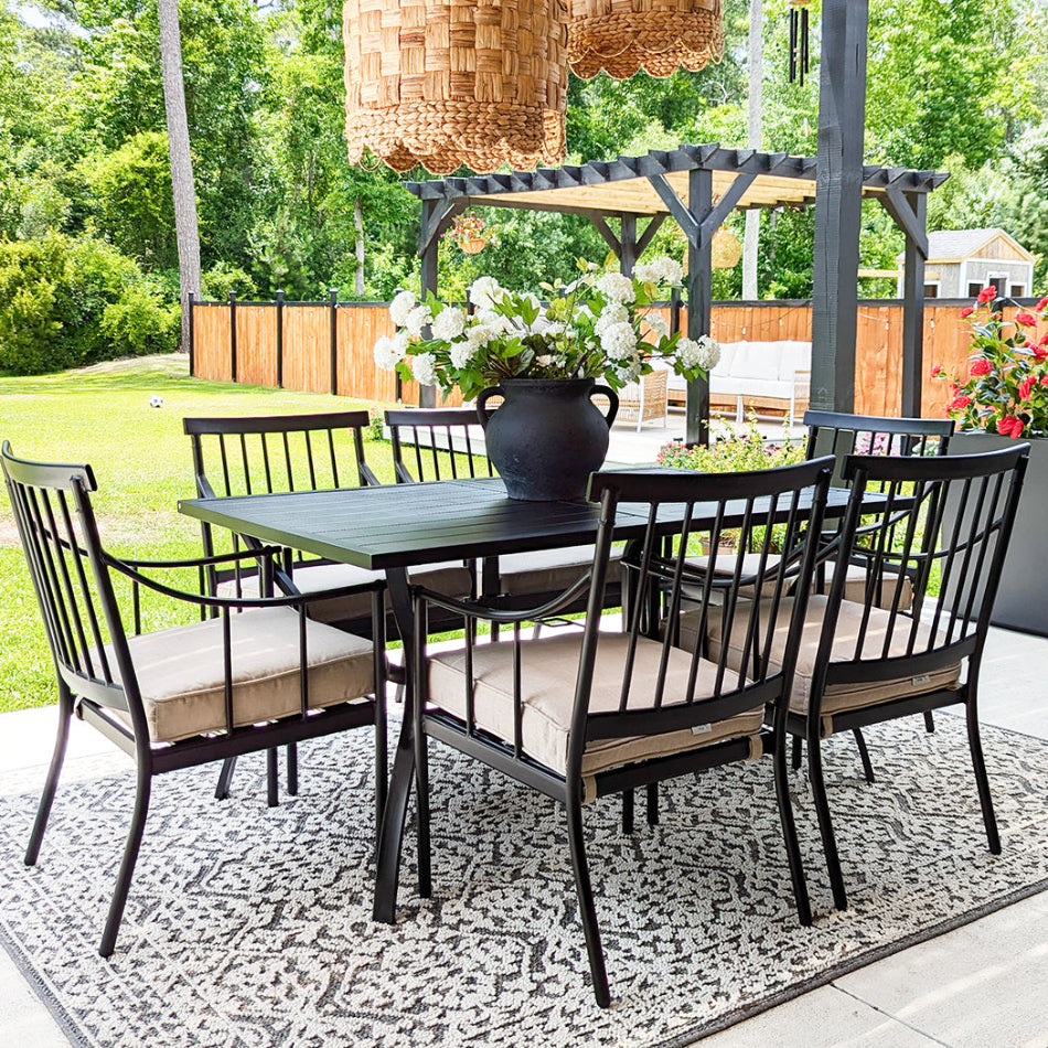 Outdoor patio set with table and chairs on a rug, surrounded by greenery.