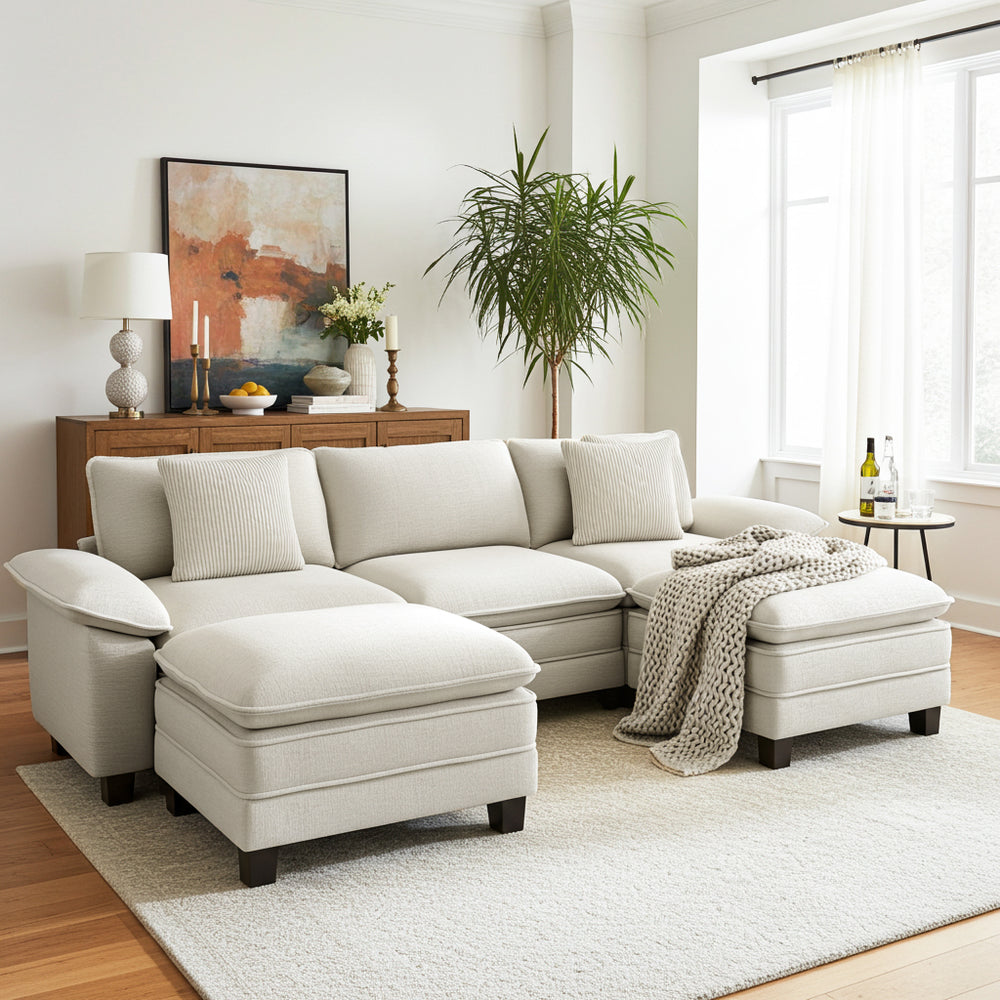Beige sectional sofa with ottoman in a living room with a side table, lamp, and artwork.