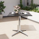 Black dining table with silver base in an outdoor setting with plants and a white wall.