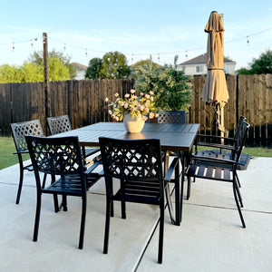 Outdoor patio set with a large square table, chairs, and an umbrella on a concrete patio.