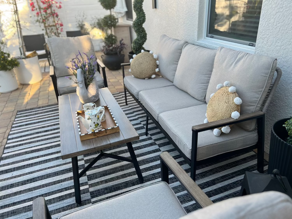 Outdoor patio with gray sofa, coffee table, and striped rug.